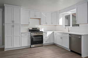 Kitchen with sink, light wood-type flooring, stainless steel appliances, white cabinets, and decorative backsplash