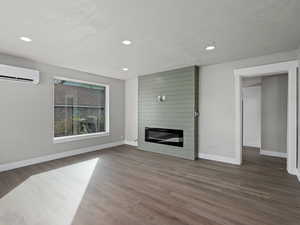 Living room with a textured ceiling, dark wood-type flooring, a large fireplace, and a wall unit AC