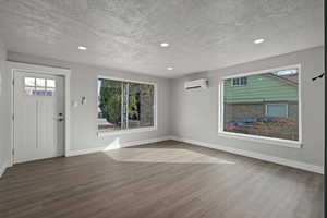 Entrance foyer featuring a wall mounted AC, a textured ceiling, plenty of natural light, and wood-type flooring