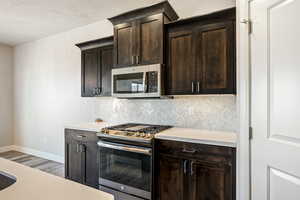 Kitchen with hardwood / wood-style flooring, stainless steel appliances, dark brown cabinetry, tasteful backsplash, and a textured ceiling