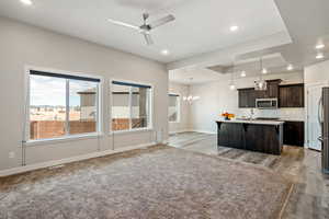 Kitchen with appliances with stainless steel finishes, a tray ceiling, decorative light fixtures, an island with sink, and dark brown cabinetry