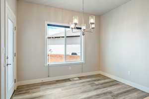 Unfurnished dining area featuring an inviting chandelier, a healthy amount of sunlight, and light hardwood / wood-style flooring