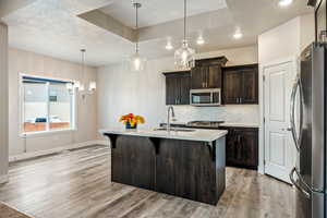 Kitchen featuring appliances with stainless steel finishes, sink, hanging light fixtures, dark brown cabinets, and a kitchen island with sink