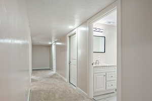 Hallway featuring a textured ceiling, sink, and light colored carpet