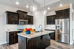 Kitchen featuring a center island with sink, a breakfast bar, dark brown cabinetry, decorative light fixtures, and appliances with stainless steel finishes