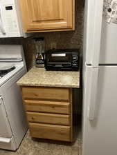 Unit 1 Kitchen with range, light stone counters, white refrigerator, and backsplash