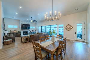 Dining room with a fireplace, light wood-type flooring, and ceiling fan with notable chandelier