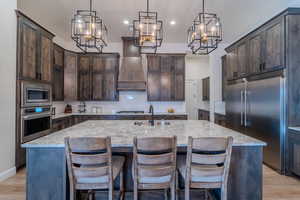 Kitchen with built in appliances, dark brown cabinetry, and a kitchen island with sink