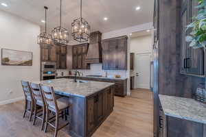 Kitchen with a kitchen island with sink, decorative light fixtures, light stone countertops, sink, and custom range hood