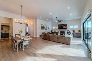 Dining area with a fireplace, ceiling fan with notable chandelier, sink, and light hardwood / wood-style flooring