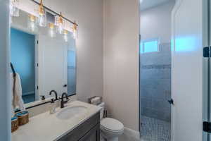 Bathroom featuring toilet, tiled shower, and vanity