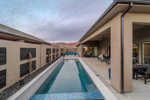 Pool at dusk featuring a mountain view, ceiling fan, and a patio