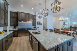 Kitchen featuring a center island with sink, appliances with stainless steel finishes, sink, light stone counters, and hanging light fixtures