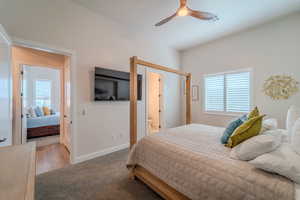 Carpeted bedroom with multiple windows, ceiling fan, and ensuite bath