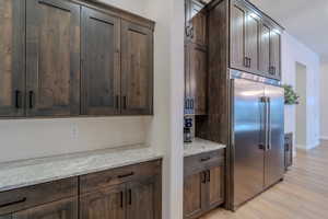 Kitchen with light wood-type flooring, dark brown cabinetry, light stone countertops, and built in refrigerator