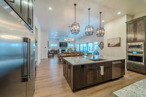 Kitchen featuring a center island with sink, dark brown cabinetry, sink, light stone counters, and appliances with stainless steel finishes