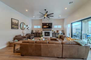 Living room with a fireplace, ceiling fan, and light wood-type flooring