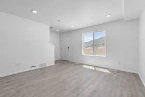 Empty room with light wood-type flooring, a mountain view, and a textured ceiling