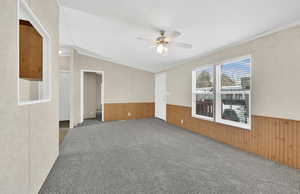 Carpeted empty room featuring ceiling fan, wooden walls, and ornamental molding