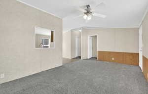 Carpeted spare room with vaulted ceiling, wooden walls, and ceiling fan