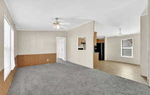 Empty room featuring wood walls, ornamental molding, light colored carpet, and ceiling fan