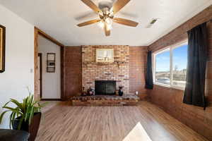 Unfurnished living room with hardwood / wood-style flooring, brick wall, a textured ceiling, ceiling fan, and a fireplace