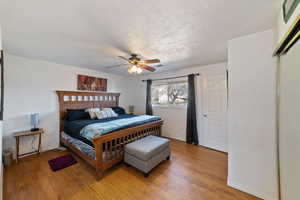 Bedroom with light wood-type flooring, a textured ceiling, ceiling fan, and brick wall