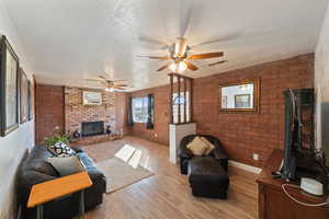 Living room with hardwood / wood-style flooring, brick wall, a brick fireplace, and a textured ceiling