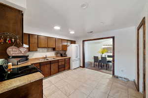 Kitchen with white fridge, sink, light tile patterned flooring, range with electric stovetop, and tasteful backsplash