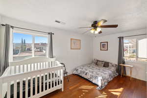 Bedroom with multiple windows, a textured ceiling, dark hardwood / wood-style flooring, and brick wall