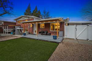 Back of property at dusk featuring brick siding, fence, a yard, a wooden deck, and a gate