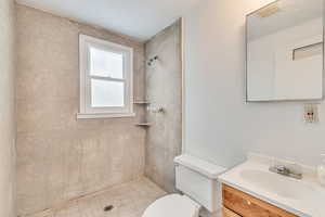 Bathroom featuring toilet, vanity, and tiled shower