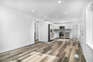 Kitchen with light hardwood / wood-style flooring, stainless steel appliances, white cabinets, and backsplash