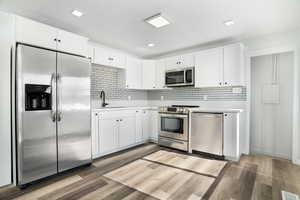 Kitchen featuring appliances with stainless steel finishes, decorative backsplash, white cabinetry, and hardwood / wood-style flooring