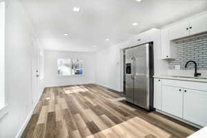 Kitchen featuring light wood-type flooring, white cabinetry, stainless steel fridge with ice dispenser, sink, and tasteful backsplash