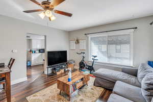 Living room with ceiling fan and dark wood-type flooring