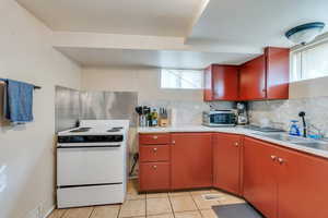 Kitchen with electric range, light tile patterned flooring, sink, and backsplash