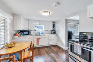 Kitchen with electric range, white cabinetry, sink, and light stone countertops