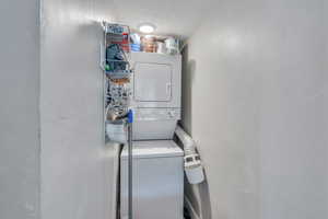 Laundry room with stacked washer and dryer and a textured ceiling