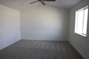 Unfurnished room with ceiling fan, vaulted ceiling, and dark colored carpet