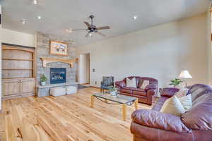 Living room featuring ceiling fan, a stone fireplace, a textured ceiling, and light wood-type flooring