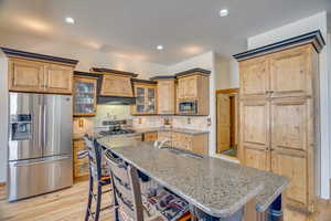 Kitchen featuring stainless steel appliances, light stone countertops, sink, and a center island with sink