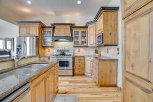 Kitchen with sink, appliances with stainless steel finishes, custom range hood, dark stone counters, and decorative backsplash