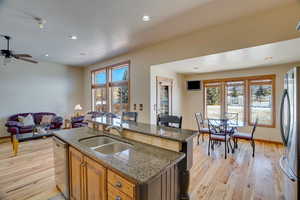 Kitchen with sink, appliances with stainless steel finishes, a kitchen island with sink, dark stone counters, and light hardwood / wood-style floors