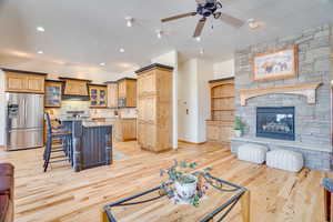 Living room featuring a stone fireplace, sink, light hardwood / wood-style flooring, a textured ceiling, and ceiling fan