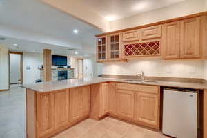 Kitchen featuring sink, stainless steel fridge, light stone countertops, a stone fireplace, and kitchen peninsula