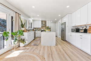 Kitchen featuring white cabinetry, a healthy amount of sunlight, appliances with stainless steel finishes, and wall chimney exhaust hood