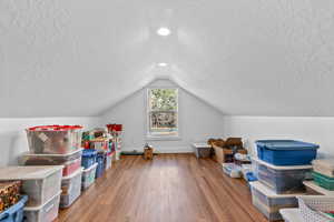 Bonus room with a textured ceiling, lofted ceiling, and hardwood / wood-style floors