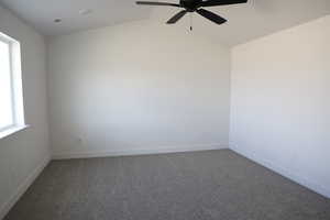 Empty room with ceiling fan, carpet floors, and lofted ceiling