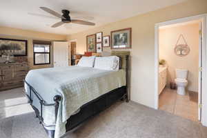 Bedroom featuring ceiling fan, light tile patterned floors, ensuite bath, and light carpet